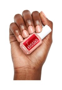 Smalto per unghie rosa chiaro in una bottiglia di vetro quadrata con un tappo bianco, tenuto in una mano con unghie smaltate dello stesso colore rosa chiaro.
