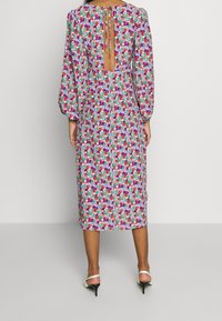 Kwiatowa sukienka o długości do połowy łydki z bufkami, wiązaniem z tyłu i odkrytymi plecami. Kolorowe wzory obejmują róż, fiolet i zieleń na jasnym tle.