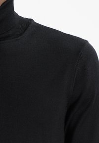 Schwarzer Rollkragenpullover mit gerippter Textur. Verfügt über ein eng anliegendes Design und einen nahtlosen Kragen. Der Stoff wirkt weich und dehnbar.
