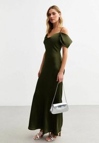 Olivegrön satin-maxikjol med avtagbara ärmar, kombinerad med en silverfärgad metallichandväska och matchande sandaletter med remmar.