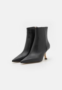 Bottines en cuir noir avec un bout pointu et un petit talon rehaussé de doré. Texture lisse et fermeture éclair simple à l'arrière.