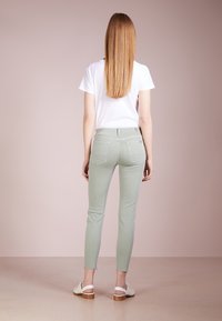 Vaaleanvihreät kapeat farkut, joissa on takataskut ja hieman repaleiset lahkeet, yhdistettynä valkoiseen t-paitaan ja vaaleisiin sandaaleihin, nähtynä takaa.