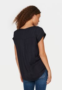 Top blu navy a maniche corte con vestibilità ampia, dotato di punti testurizzati e schiena aperta, abbinato a jeans in denim blu chiaro.