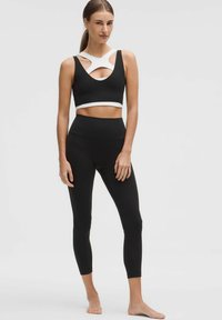 Conjunto de ropa deportiva negra que incluye una camiseta sin mangas corta con acentos blancos y detalles recortados, combinada con leggings de cintura alta, ambos en una textura suave.