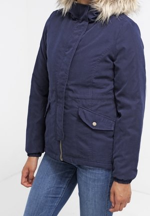 Marineblå parka-jakke med faux fur hætte, lynlås, sidelommer og elastiske manchetter, der fremhæver et blødt, struktureret stof.