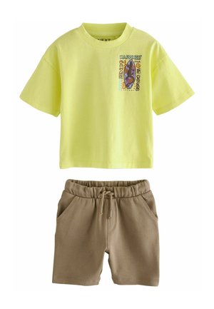 Gelbes Baumwoll-T-Shirt mit grafischem Druck und kurzen Ärmeln, kombiniert mit braunen Shorts mit Kordelzug aus weichem Material.