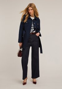 Navy zewnętrzny płaszcz z złotymi guzikami, biała i granatowa koszula w paski, ciemne szerokie dżinsy, połączone z burgundowymi szpilkami i torebką.