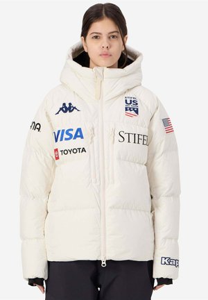 Giacca piumino bianca con cappuccio, caratterizzata da loghi in blu e nero, tra cui Kappa e US Ski Team. Chiusura con zip e tasche laterali con zip.