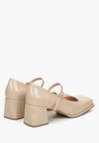 Beżowe, lakierowane buty na słupku z kwadratowym noskiem i paskiem z zapięciem przy kostce.