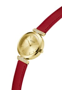 Reloj de oro con una esfera texturizada, índices de hora dorados y una correa de cuero roja. Acabado con adornos de cristal cerca de las asas.