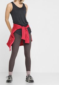Canotta nera, felpa rossa annodata in vita, leggings marroni e scarpe da ginnastica nere con accenti grigi. Look atletico informale.