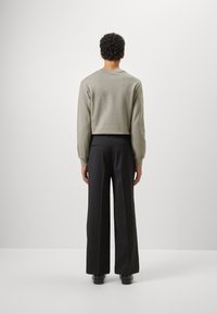 Světle šedá zkrácená mikina v kombinaci s černými širokými kalhotami. Mikina má přiléhavé rukávy a kulatý výstřih. Hladké textury po celé ploše.