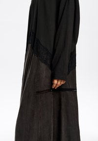 Długa czarna sukienka z koronkowymi akcentami. Górna część jest teksturowana, dolna gładka z plisowanym wzorem. Posiada skomplikowane koronkowe wykończenia i przeszycia.