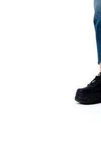 Right leg wearing blue jeans and black platform sneaker, standing on white background.