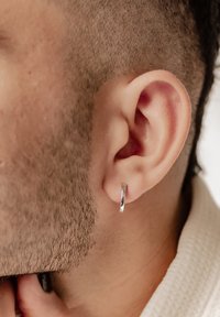 Pendiente de aro plateado exhibido en una oreja recortada, que presenta una superficie suave y brillante y un diseño circular simple.