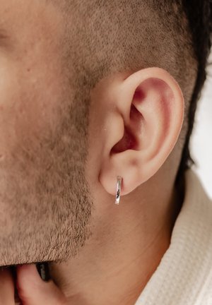 Silberner Creolenohrring, der an einem kurz geschorenen Ohr präsentiert wird, mit einer glatten, glänzenden Oberfläche und einem einfachen kreisförmigen Design.