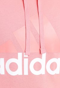 Ljust rosa sweatshirt med huva, med vit "adidas" logotyp och triangulära designelement. Bomullstyg, synliga dragsko.