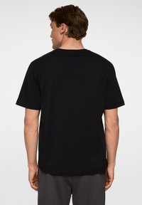 Mustan lyhytnokkaisen t-paidan, joka on valmistettu puuvillasta, rento istuvuus ja pyöreä pääntie, katsottuna takaa, sileä pinta.