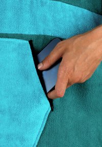 Handtuch mit abwechselnden turquoise und teal Streifen, ausgestattet mit einer Tasche, in die eine Hand ein dunkel gefärbtes Mobilgerät legt. Strukturiertes Gewebe.
