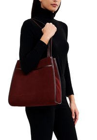 Borsa a spalla bordeaux con una superficie in suede liscia, bordatura in pelle a contrasto e doppio manico. Caratterizzata da una tasca frontale per lo stoccaggio.