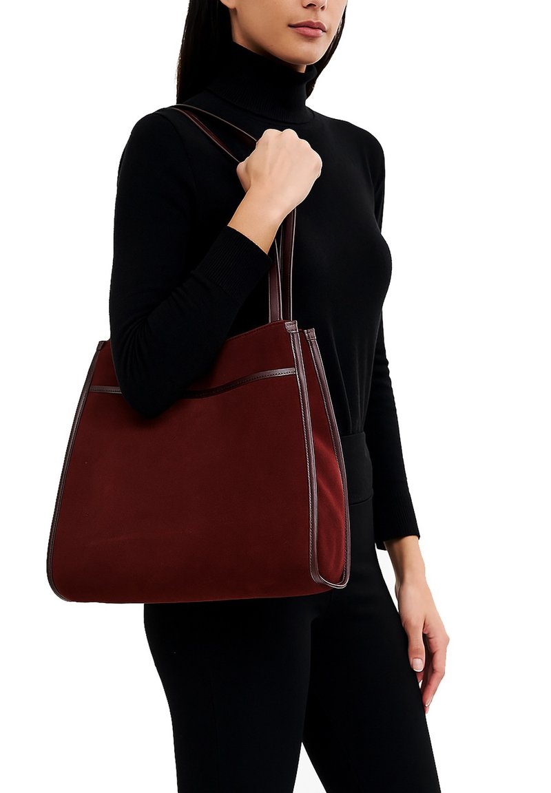 Borsa a spalla bordeaux con una superficie in suede liscia, bordatura in pelle a contrasto e doppio manico. Caratterizzata da una tasca frontale per lo stoccaggio.