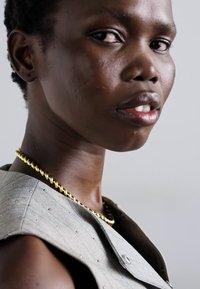 Vêtement en tissu gris avec un motif texturé, arborant un collier torsadé doré qui met en valeur le décolleté et les détails de couture visibles.