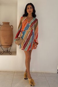 Spalvinga suknelė su vertikaliomis oranžinės, turkio ir rudos spalvų juostelėmis ir auksinėmis dėmėmis, derinama su geltonais tekstūruotais batais ir smėlio spalvos rankine.