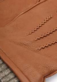 Bruine leren handschoen met een gestructureerd oppervlak, decoratieve stiklijnen en een zachte gebreide boord. Soepele afwerking met een natuurlijk nerfpatroon.