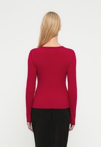 Top a maniche lunghe a coste di colore rosso scuro, con un design aderente e una scollatura rotonda, dalla texture liscia.