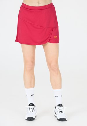 Röd sportkjol med lagerdesign, elastisk midja och en liten gul "FZ"-logotyp på sidan. Bärs med vita strumpor och sportskor.
