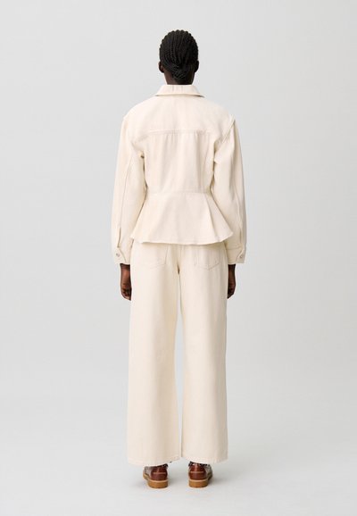 Conjunto de dos piezas que incluye una chaqueta peplum ajustada de color crema con mangas largas y pantalones de pierna ancha a juego. Textura suave, detalles mínimos.