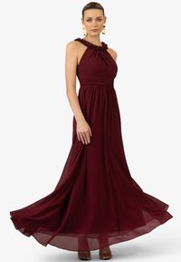Burgundowa sukienka maxi na ramiączkach z falbaną przy dekolcie i plisowanym korpusem. Płynący materiał z szyfonu o lekkim połysku, tworzący elegancką draperię.