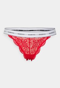 String rouge en dentelle avec motifs floraux, bords festonnés et une ceinture élastique blanche avec le logo "GUESS" imprimé en noir.