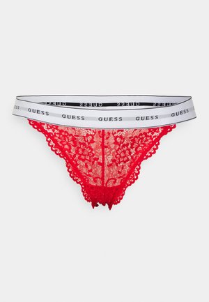 Punainen pitsinen stringi, jossa on kukkakuviot, hapsureunat ja valkoinen joustovyötärö, johon on painettu mustalla "GUESS" -logo.