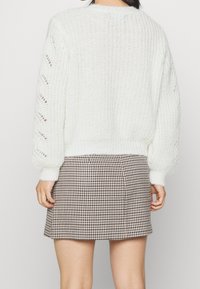 Vit stickad tröja med långa ärmar som har hålmönster; kombinerad med en kort brun hundtandsmönstrad kjol.