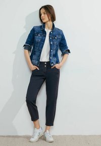 Jeansjacka i mörkblått med klassisk krage och två bröstfickor, matchad med marinblå byxor med dubbelknappdesign och vita sneakers.