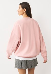 Veľká ružová mikina s rebrovaným výstrihom a manžetami, v kombinácii s plisovanou čierno-bielou sukňou so vzorom psieho zubu.