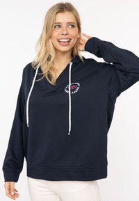 Granatowy fason z kapturem ze białymi sznurkami, projekt z dekoltem w serek oraz okrągłym haftowanym logo w różowym i białym kolorze, na którym widnieje słowo "Happy."