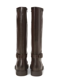 Des bottes en cuir marron jusqu'au genou présentent une finition lisse, une fermeture éclair sur le côté et une sangle décorative avec une boucle au niveau de la cheville.