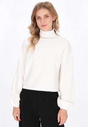 Weißer, kurzer Rollkragenpullover mit langen, puffigen Ärmeln. Weiche Textur und gerippter Kragen. Kombiniert mit schwarzen Hosen, minimalistisches Design.