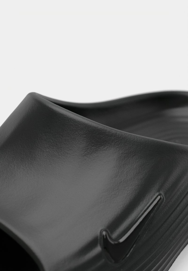 Zwarte instapper met een glanzende afwerking, voorzien van een ronde bovenkant en een textuur inlegzool, accenten met een klein zwart logo detail aan de zijkant.