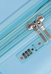 Lichtblauwe koffer met rits, voorzien van twee metalen ritshandvatten en een ingebouwde TSA-combinatieslot met code "000".