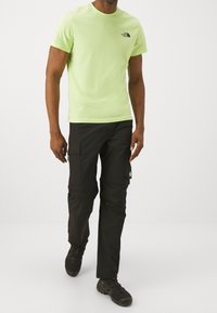 Pánské krátkoslé t-shirt neonově zelené barvy s kulatým výstřihem, v kombinaci s černými cargo kalhotami s bočními kapsami a decentním logem.