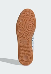 Gum krāsas gumijas apavu zole ar teksturētu dizainu, kas ietver apaļas un lineāras formas. Ieliekts logo centrā.