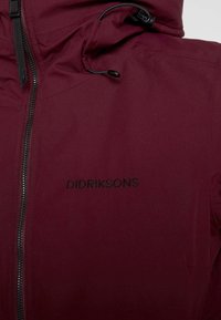 Burgundská nepromokavá bunda se zipem, která má kapuci, nastavitelné stahovací šňůrky a vyšitý logo "Didriksons" na hrudi.