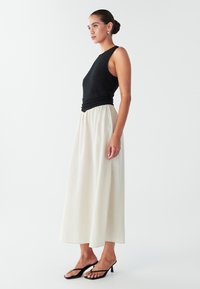 Mustast ribastatud varrukateta top koos kogutud vööosaga, kombineeritud voolava elevandiluu värvi seelikuga. Täiendatud mustade kontsadega sandaalidega.