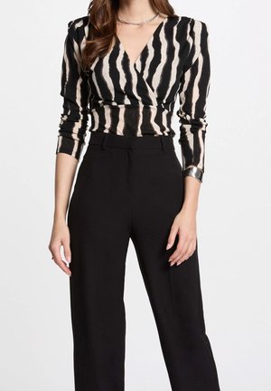 Vrouw draagt zwarte broek met hoge taille en wijde pijpen en een zwart-beige zebraprint top met lange mouwen, zilveren armband en ketting.