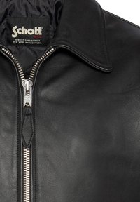 Schwarze Lederjacke mit gesteppter Innenfütterung, spitzem Kragen und silbernem Reißverschluss mit gebrandetem Zipper. Markante Textur und Design.