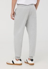 Pantaloni sportivi grigi con cintura elastica, tasche laterali e polsini a coste, abbinati a sneaker bianche con dettagli neri.