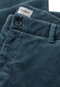 Dunkelblaugrüne Corduroyhose mit vertikal gerippter Textur. Verfügt über einen schwarzen Knopf und ein hessnatur-Label am Bund.